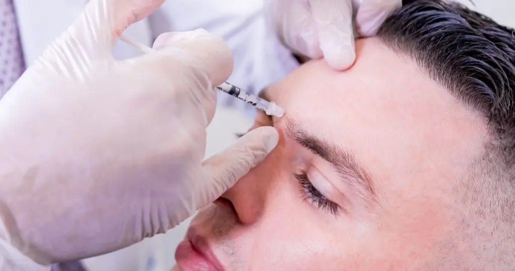 Close-up of a man receiving a cosmetic injection of Neurotoxins in Albuquerque, NM in his forehead area by a professional in white gloves.