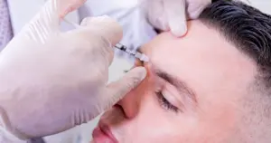 Close-up of a man receiving a cosmetic injection of Neurotoxins in Albuquerque, NM in his forehead area by a professional in white gloves.